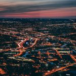 Aerial night view of Boston, MA with glowing city streets and highways stretching to the horizon at dusk.